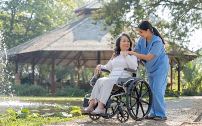 Young female in uniform with senior patient in a wheelchair chilling out in park.