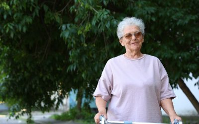 Elderly woman using walking frame in park. Space for text